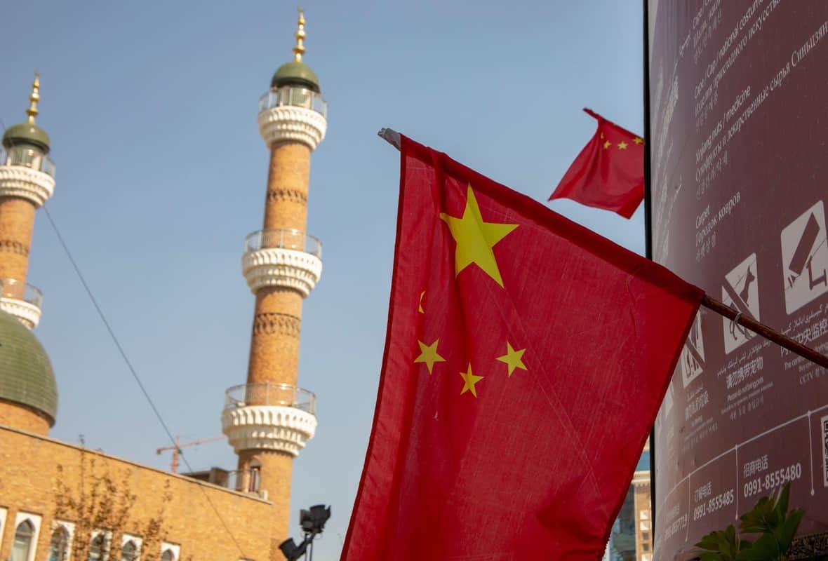 A photo of a Chinese flag in front of a minaret and a sign showing surveillance cameras
