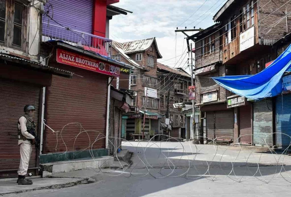 Soldier standing guard in a Kashmir street divided by barbed wire in Aug 2020 on the anniversary of the internet shutdown starting