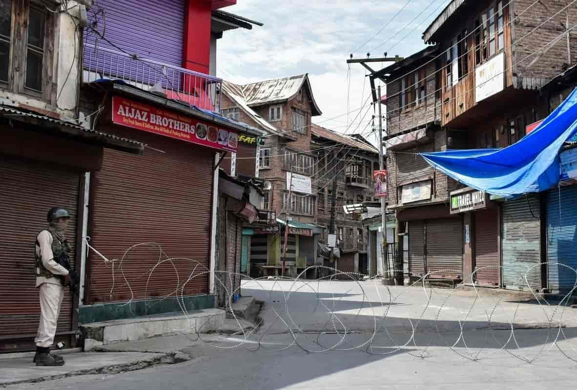 On the anniversary of the start of the Kashmir internet shutdown, a soldier stands guard in a street divided by barbed wire in Aug 2020