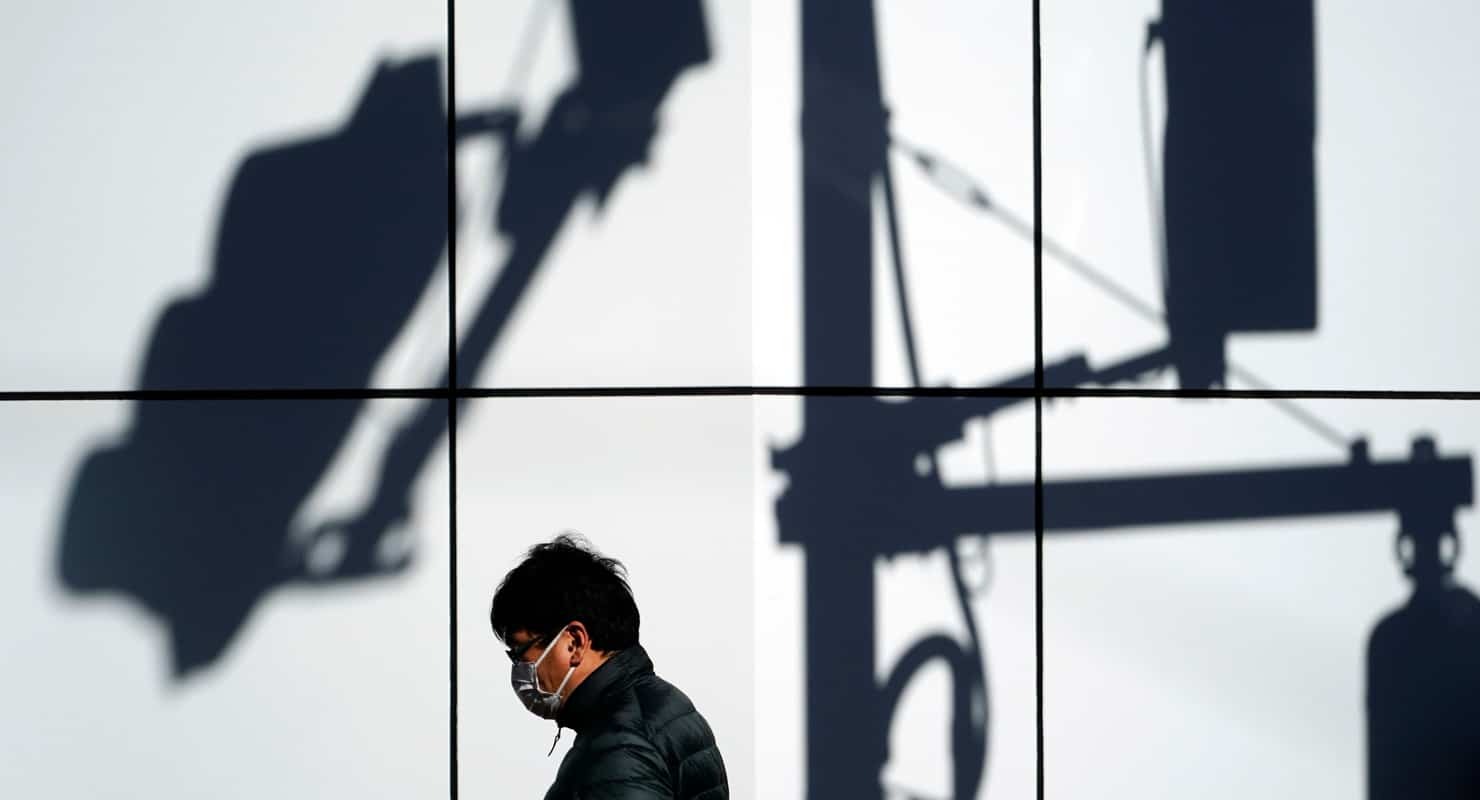 Photo of a man walking in shadow of surveillance cameras, it's the main image for the "Privacy Tracker: Contact Tracing & Digital Health Certificate Apps" report.