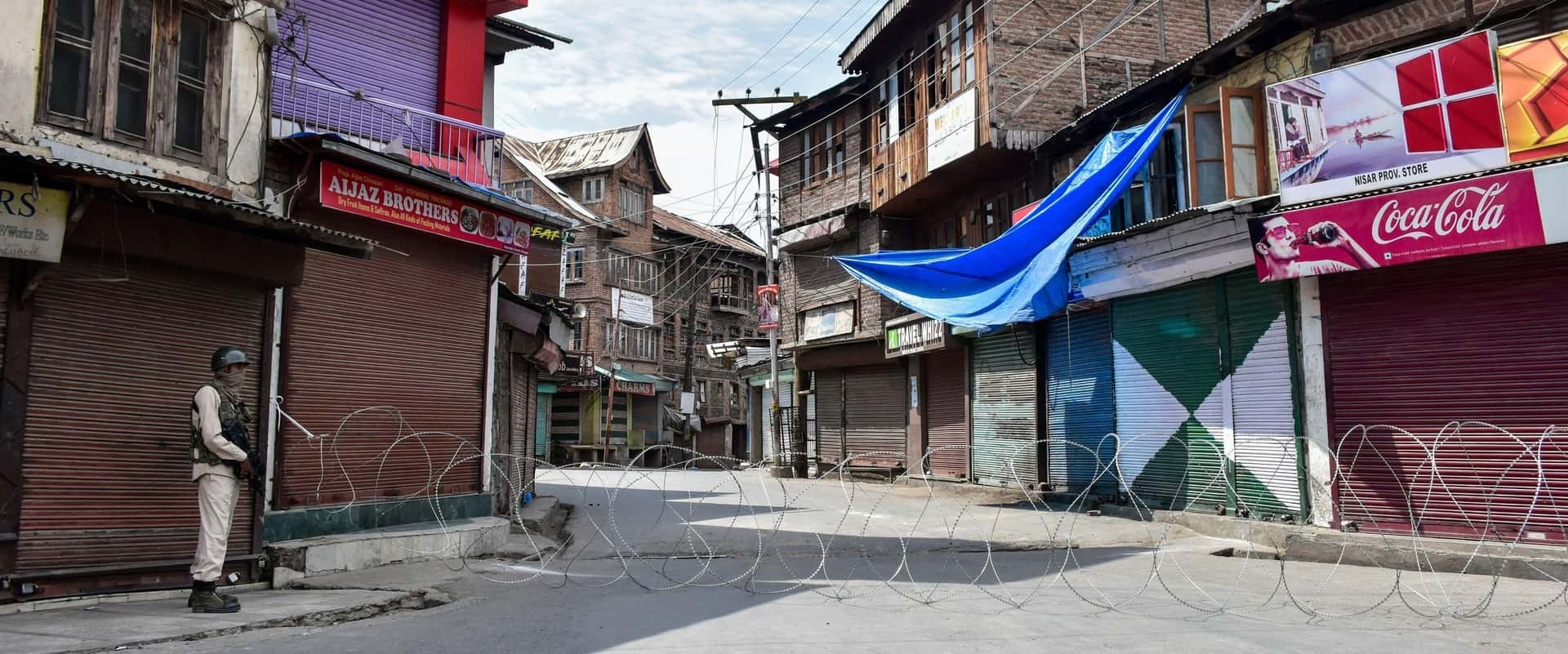 Soldier standing guard in a Kashmir street divided by barbed wire in Aug 2020 on the anniversary of the internet shutdown starting