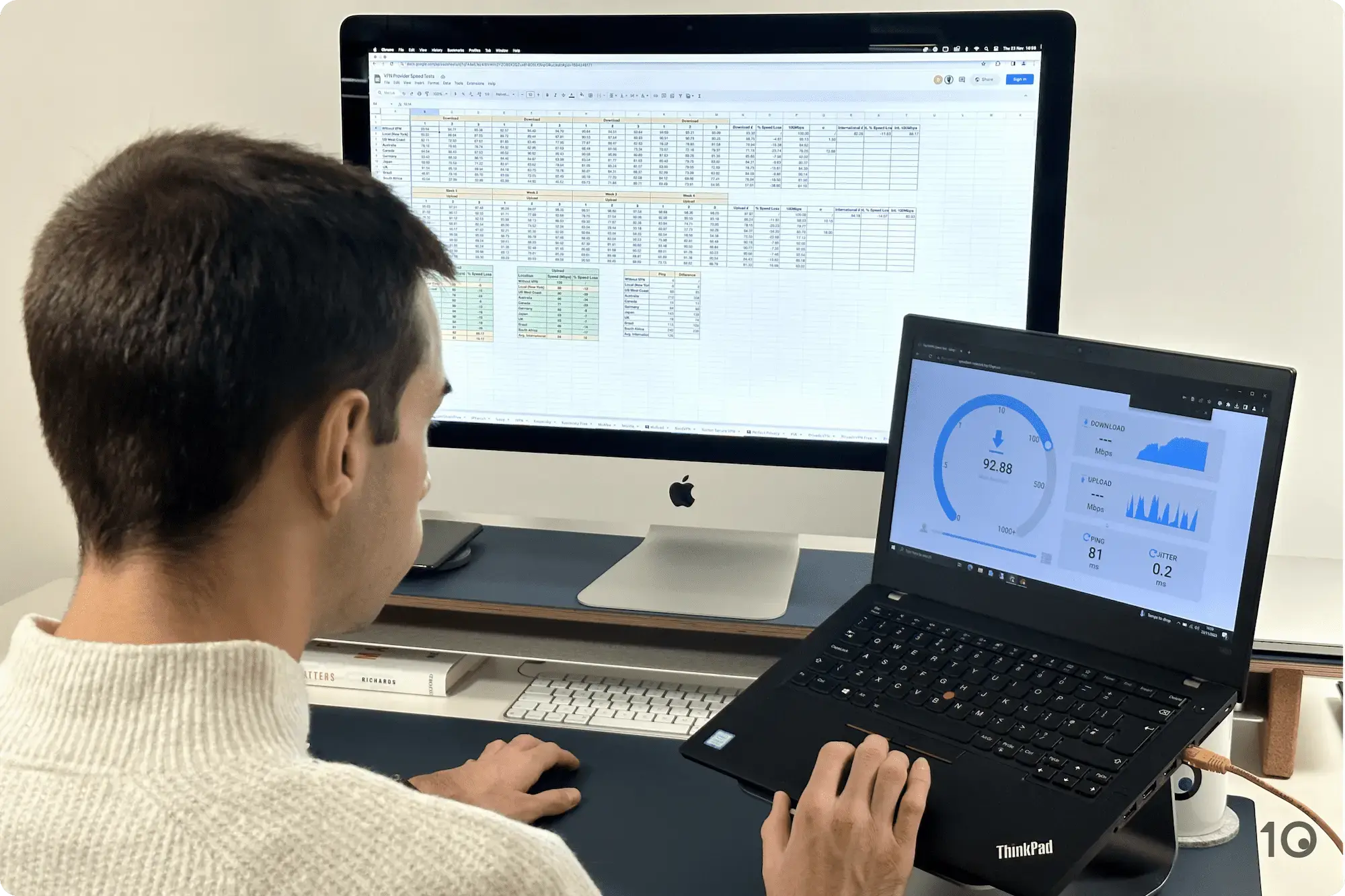 Un homme assis à un bureau teste les performances de vitesse d'un VPN sur un ordinateur portable et analyse une feuille de calcul des résultats des tests de vitesse sur un iMac.